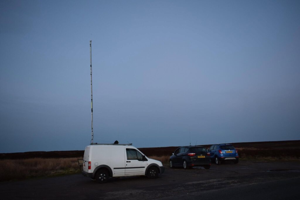 A van with an antenna mast in a field